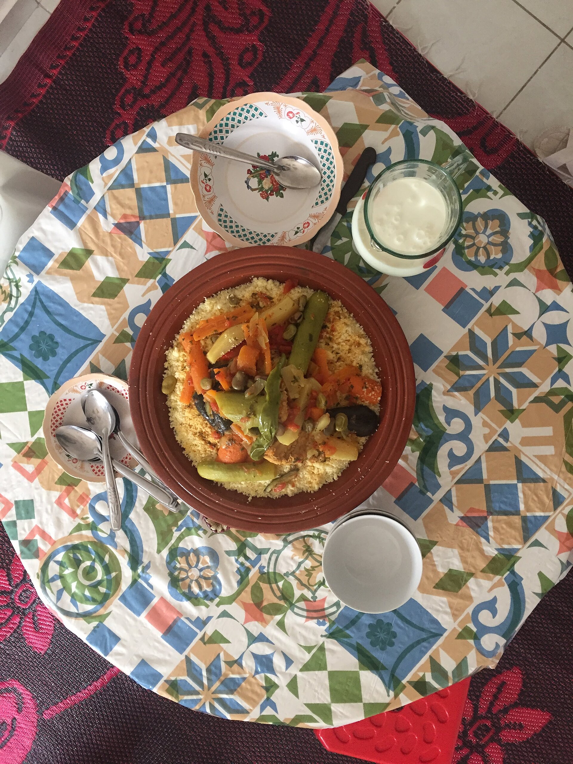A communal couscous platter shared at a Moroccan Friday family lunch, surrounded by hands eating from sections nearest each diner.