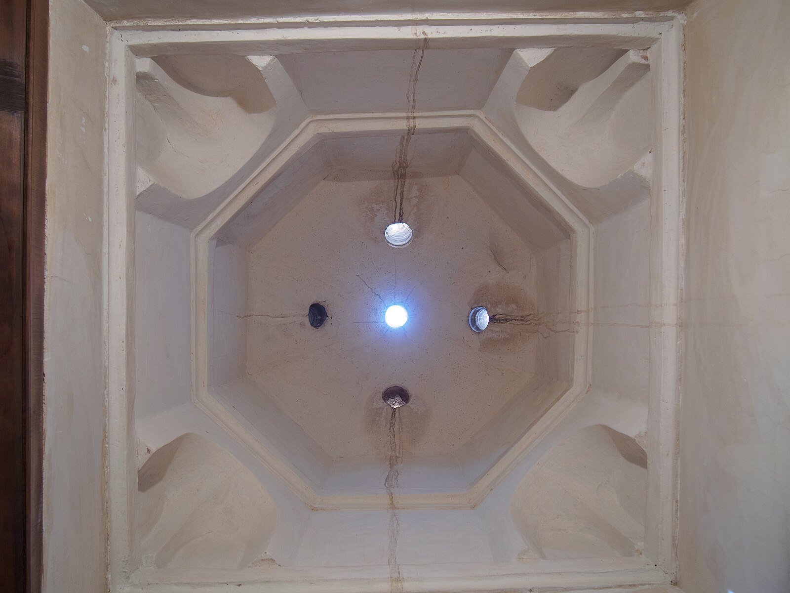 Vaulted interior of a Moroccan hammam at the Bahia Palace in Marrakech, with light filtering through star-shaped openings in the dome.